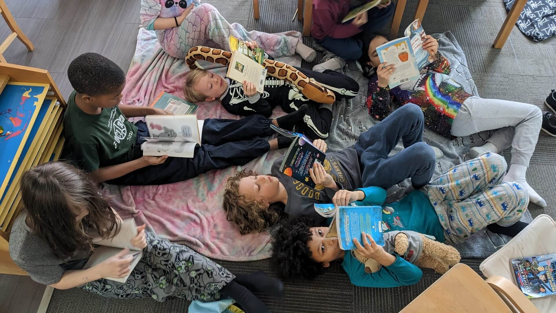Four Corners Montessori Academy students laying down and reading during the Pajama Reading Day in the classroom.